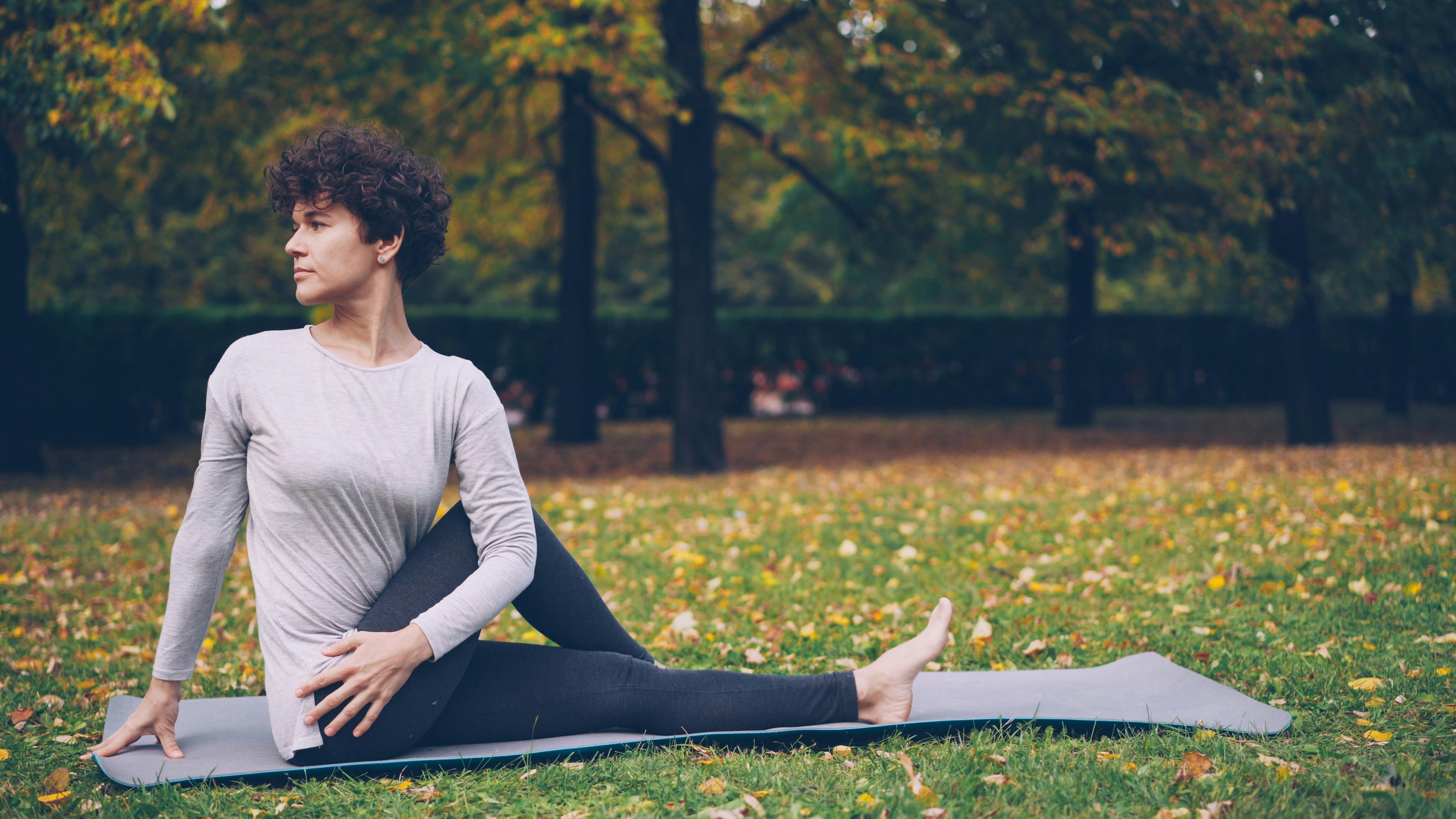 A woman doing yoga on a mat in a park surrounded by autumn foliage. Ideal for lifestyle and health themes.