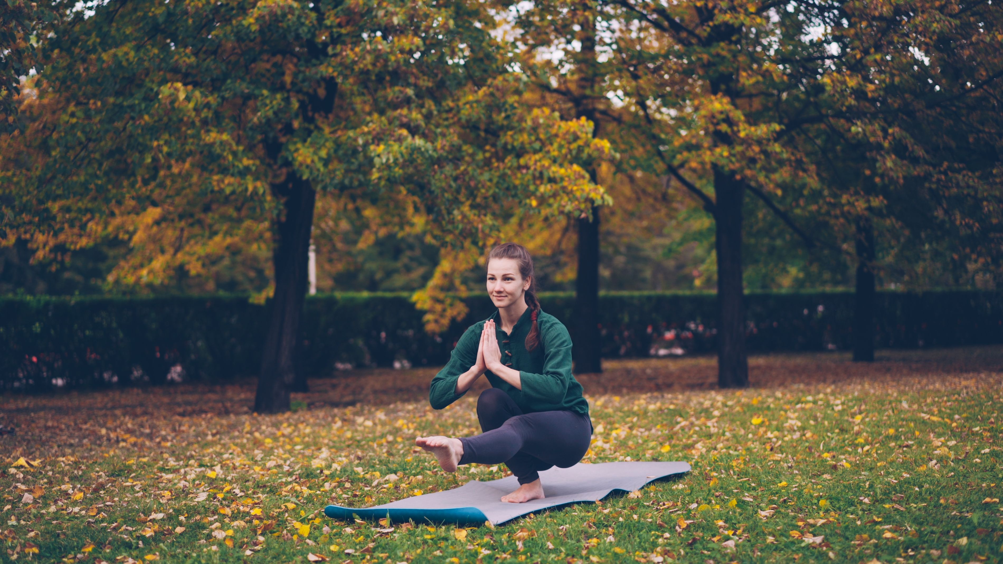 Woman in yoga pose outdoors with autumn foliage, serene exercise setting.