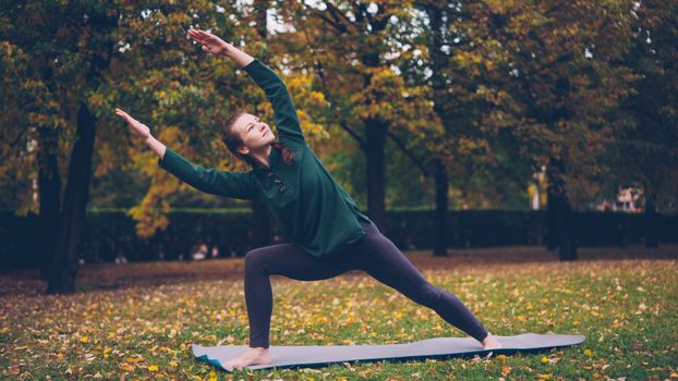Woman performing yoga on a mat in a park during fall.