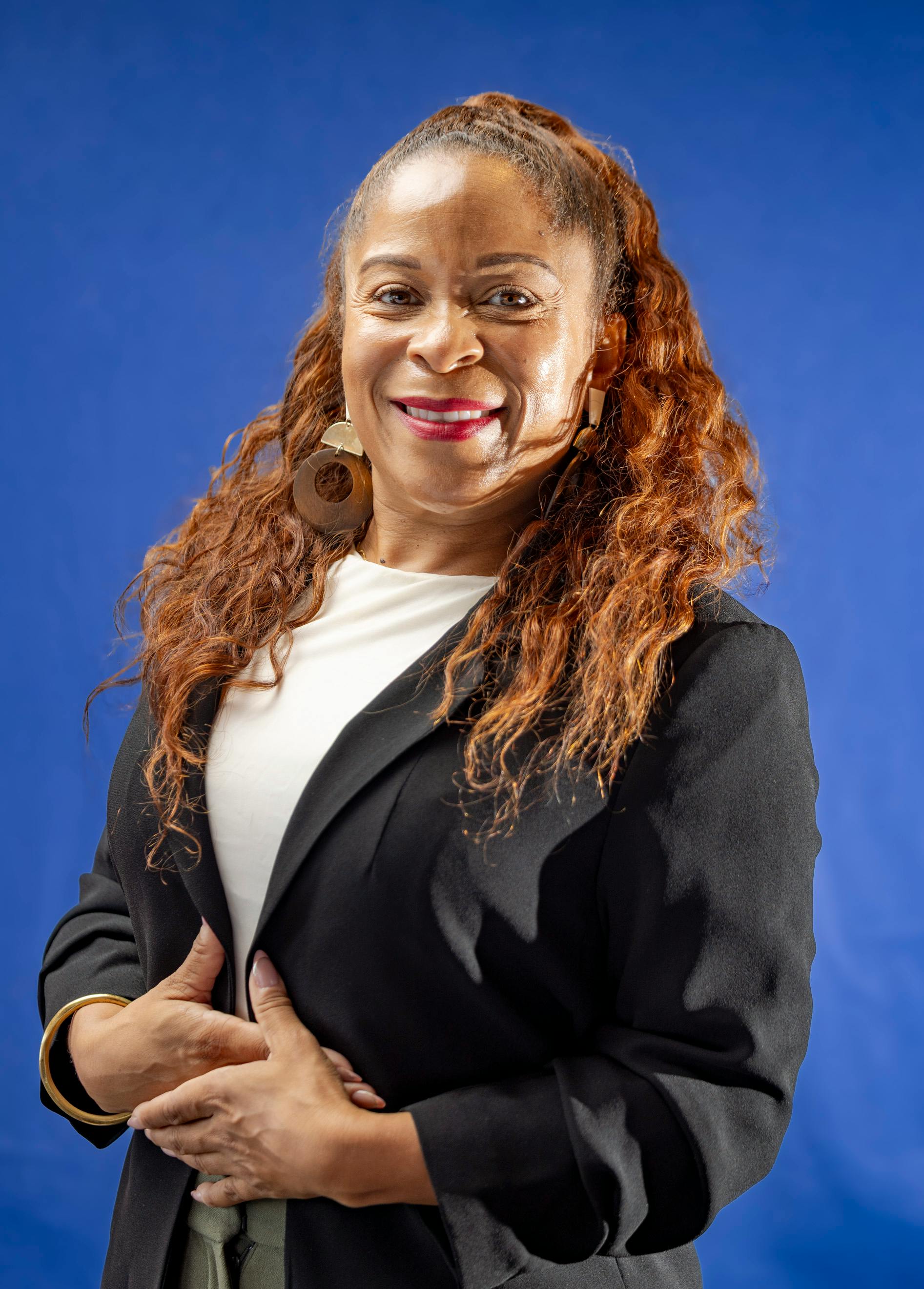 Smiling woman in business attire with blue backdrop, exuding confidence.