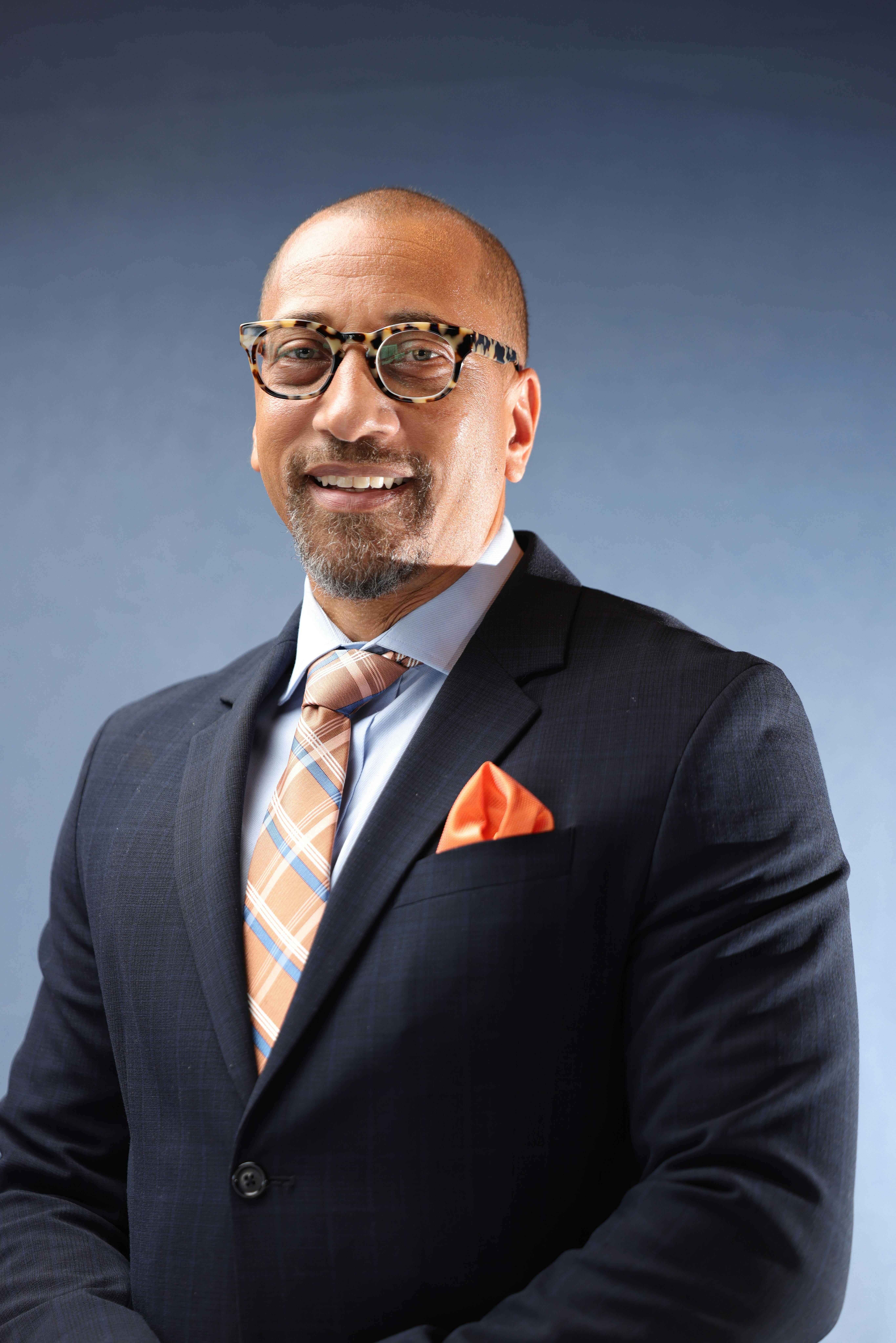 Confident businessman in suit and tie smiling against a blue background.