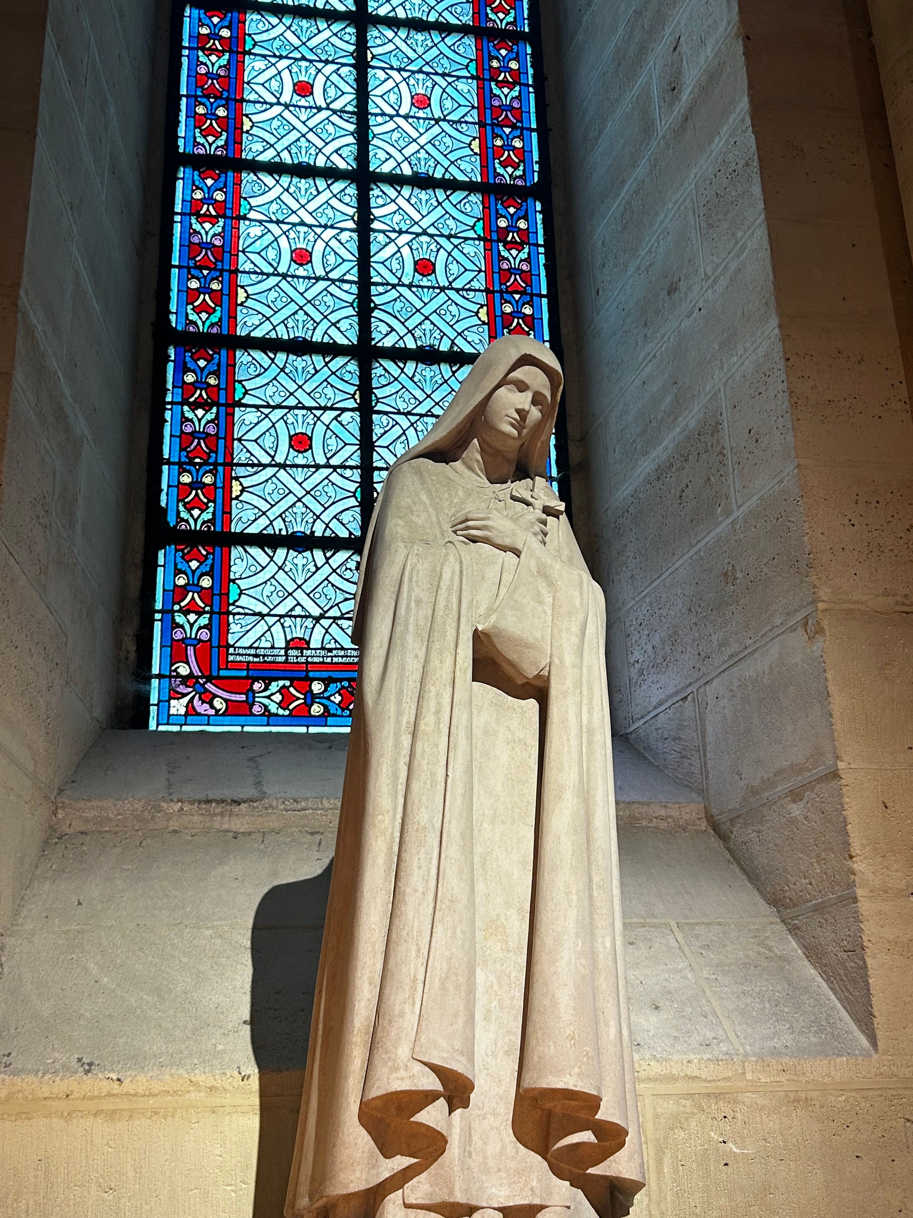 A serene statue inside a Paris cathedral with vibrant stained glass.