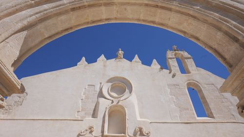 Free Photography of a historic stone arch and facade with a clear blue sky, capturing heritage architecture. Stock Photo