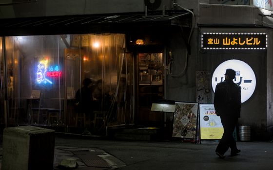 A man silhouetted against a neon-lit Osaka restaurant at night.