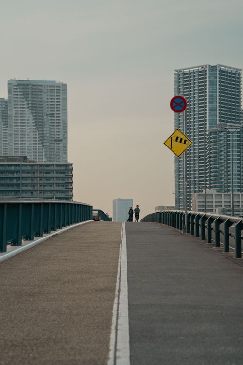 Free A modern bridge in Tokyo, Japan, with silhouetted figures and skyscrapers in the background. Stock Photo