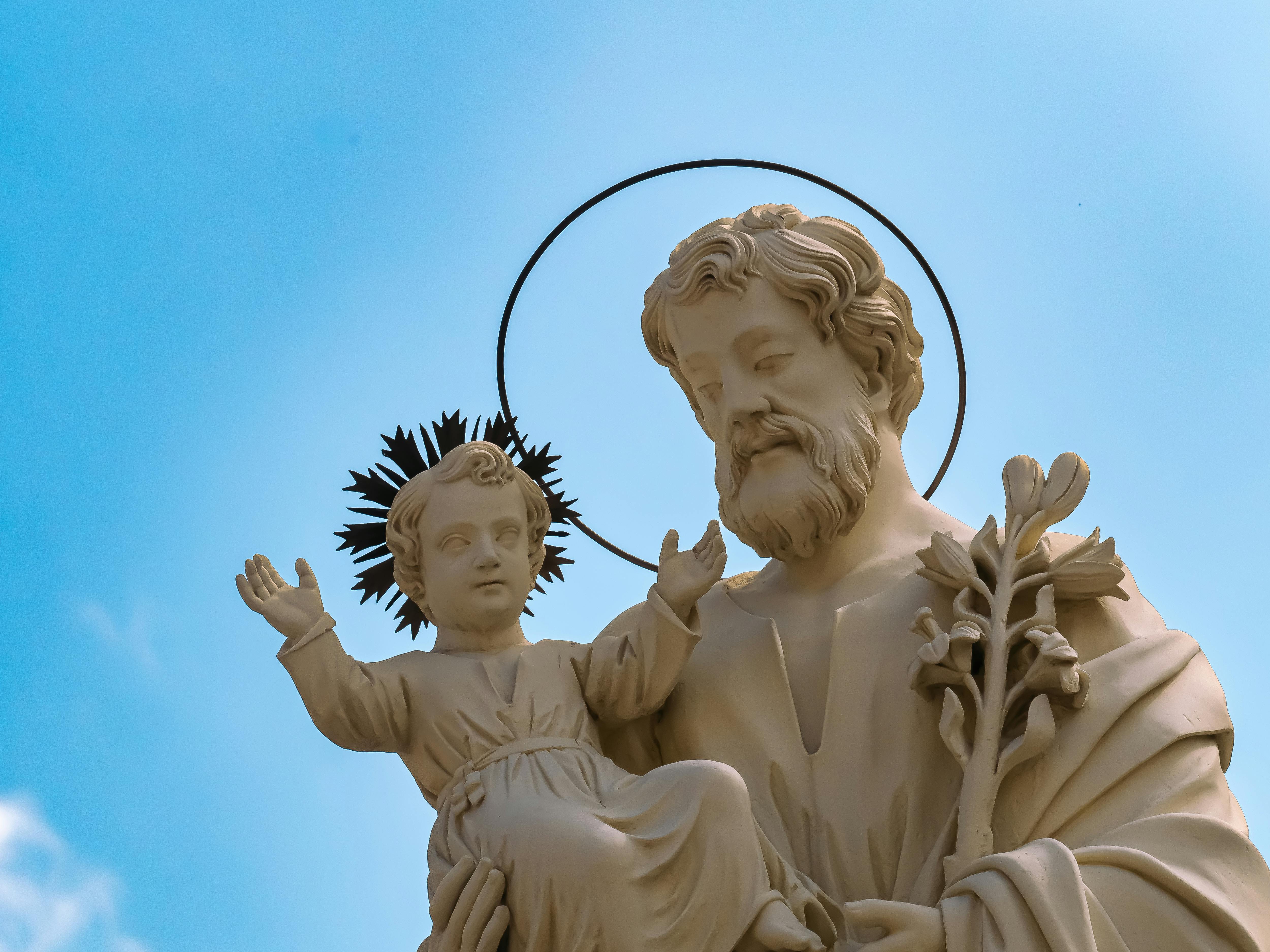 A detailed statue of Saint Joseph holding a child, set against a clear blue sky.