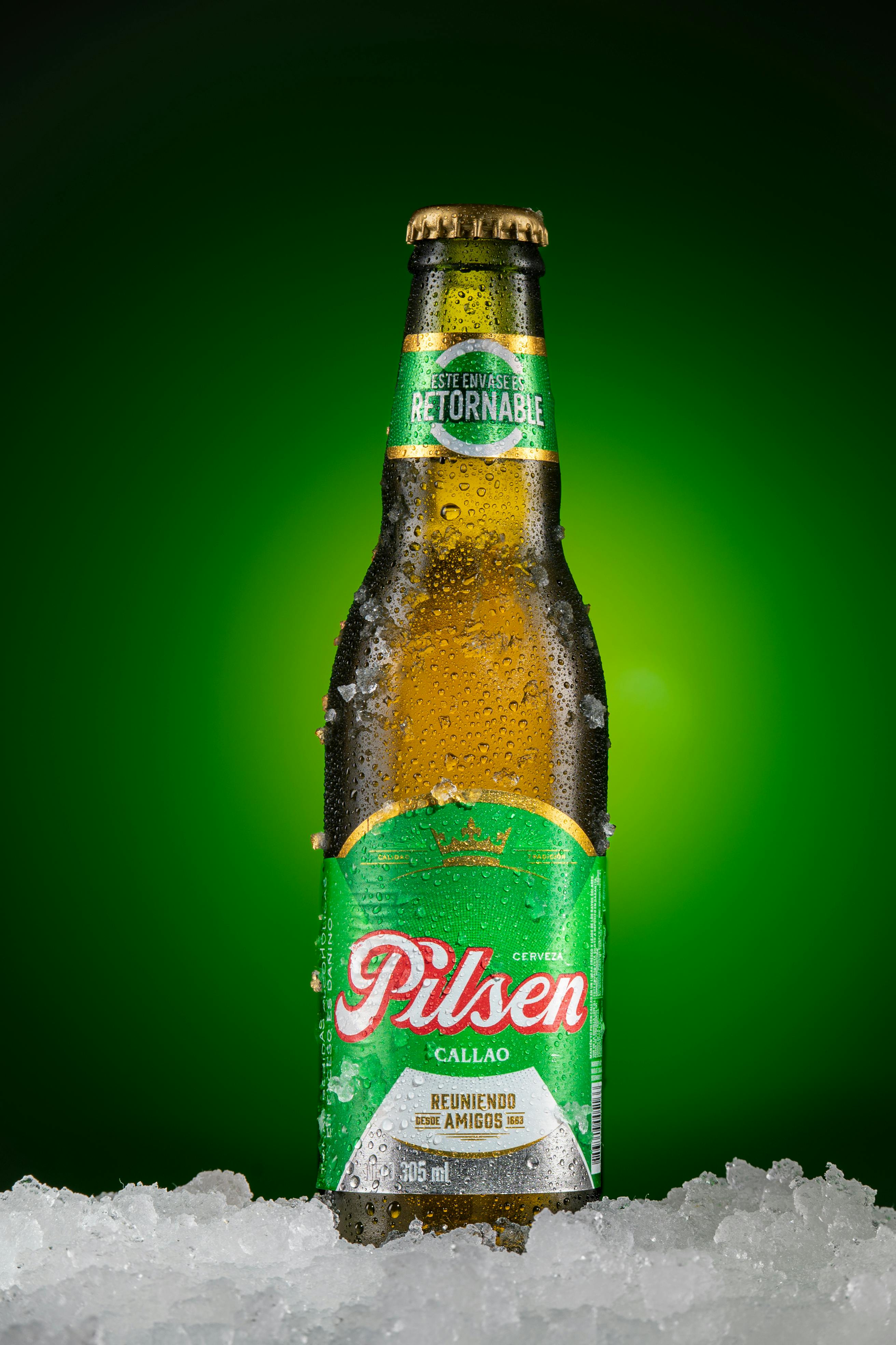 Beaded Pilsen Callao beer bottle on ice with vibrant green glow.
