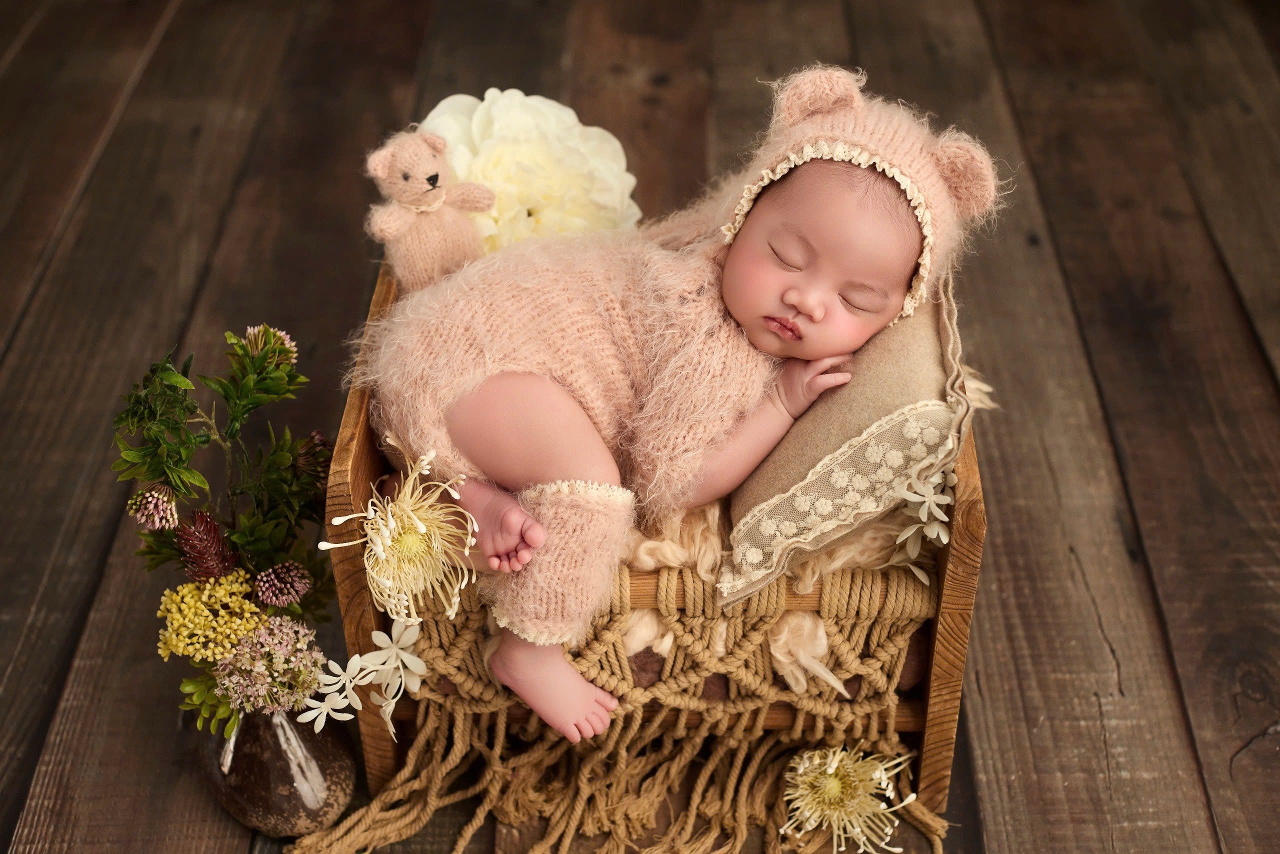 Cute baby peacefully sleeping in wooden basket, wearing a fluffy teddy bear costume.