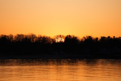 Free A tranquil sunset with vibrant hues reflecting on calm waters, silhouetted by trees. Stock Photo