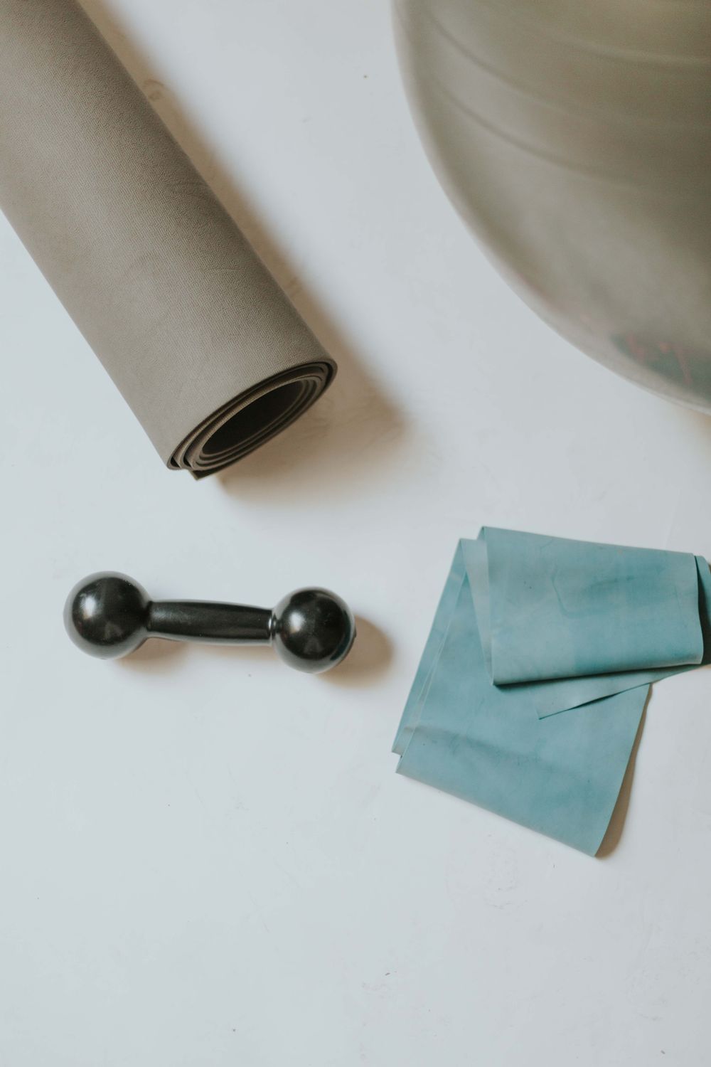 Flat lay of home workout equipment with a mat, exercise ball, resistance band, and small training tools