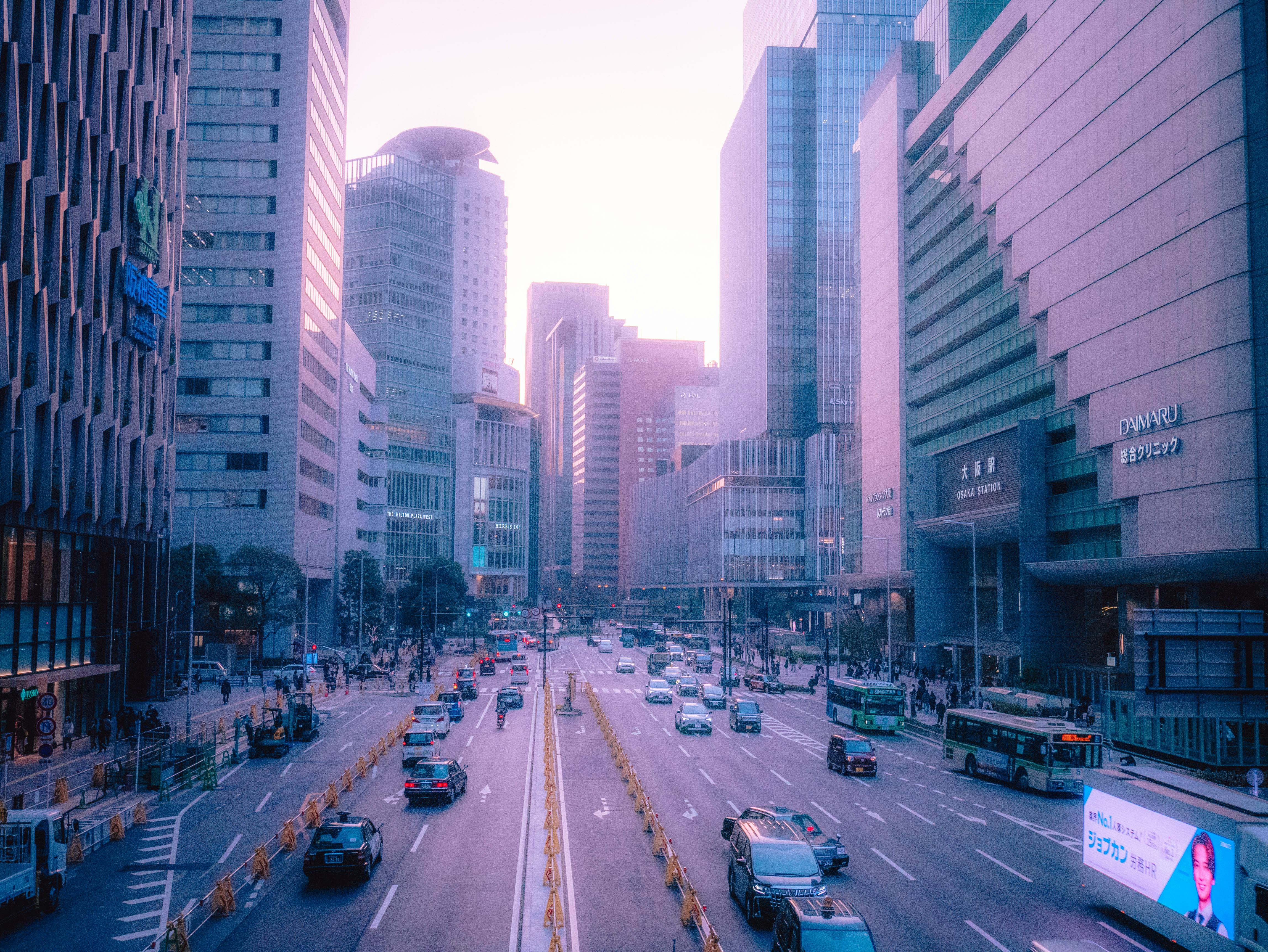 Pohled z výšky na rušnou ulici v Ósace v Japonsku s moderními mrakodrapy, dopravou a chodci během jemného západu slunce v purpurových tónech.