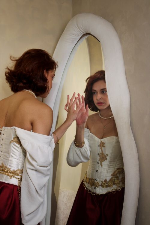 Free A woman in a corset looks at her reflection in an elegant mirror, indoors. Stock Photo