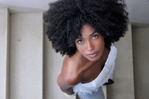 Free Elegant portrait of a woman with afro hairstyle looking up from staircase. Stock Photo