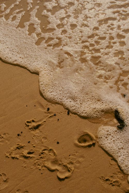Free Footprints captured on a sandy beach as ocean waves gently wash over them. Stock Photo