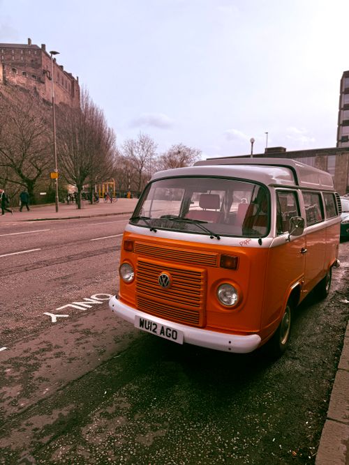 Free Classic orange van parked near Edinburgh Castle on a clear day in Scotland, showcasing urban charm and historical background. Stock Photo