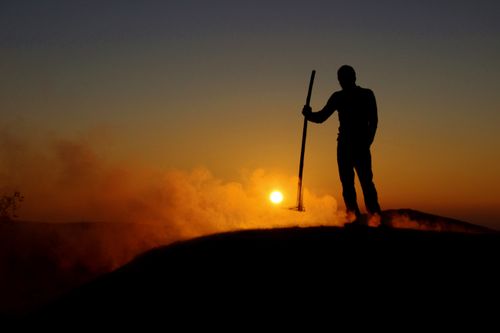 Free A striking silhouette of a person holding a tool against a smoky sunset sky. Stock Photo