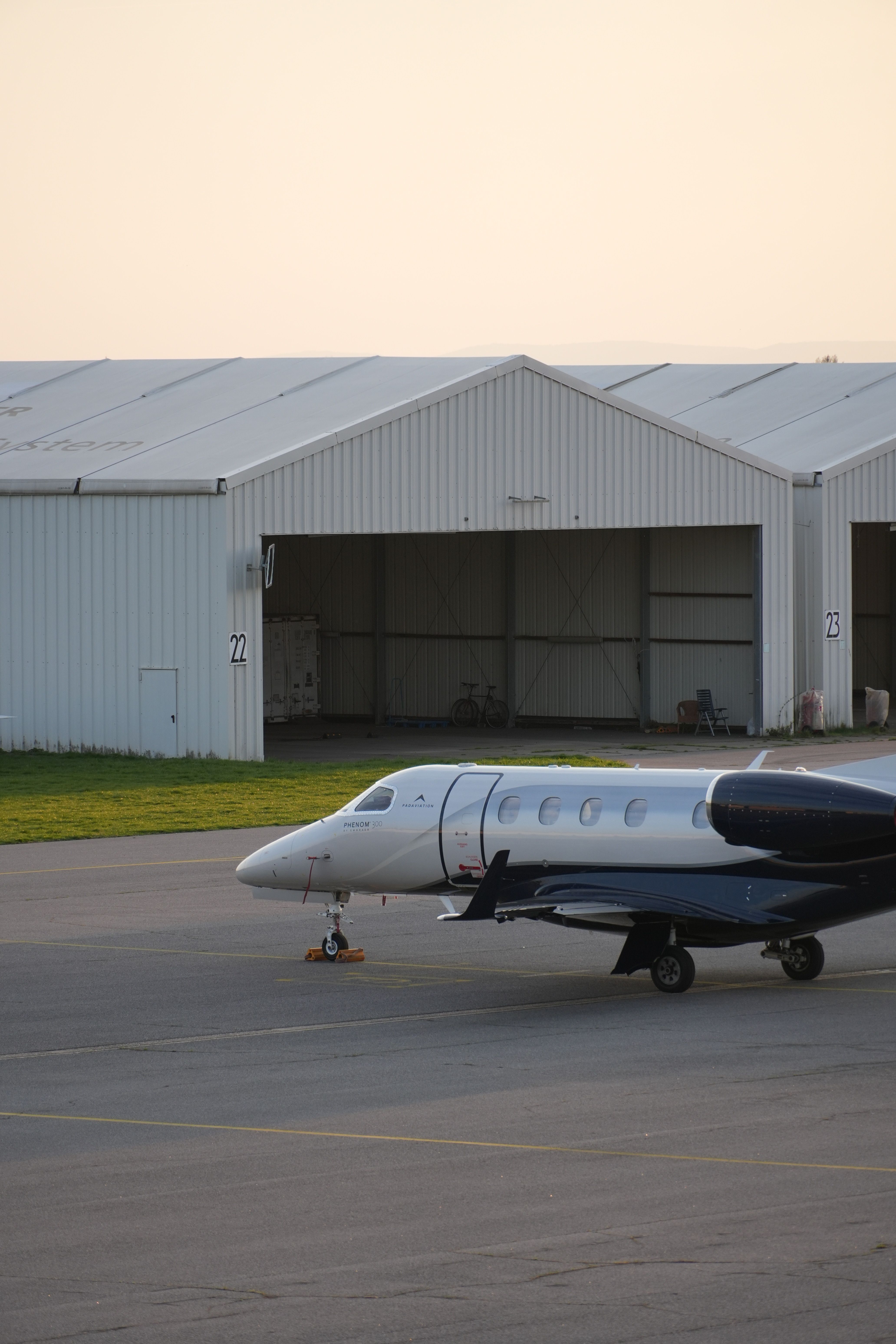 A sleek private jet rests on the tarmac in front of aircraft hangars during daytime.