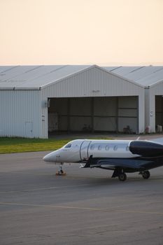 A sleek private jet rests on the tarmac in front of aircraft hangars during daytime.
