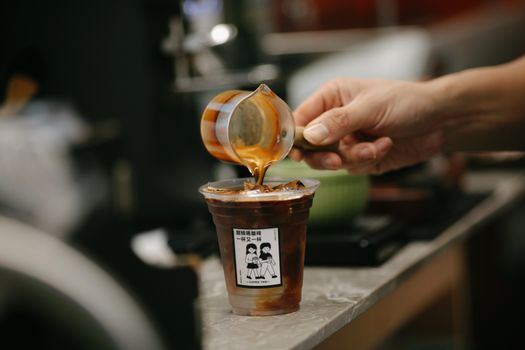 Close-up of caramel syrup being poured over iced coffee in a café setting.