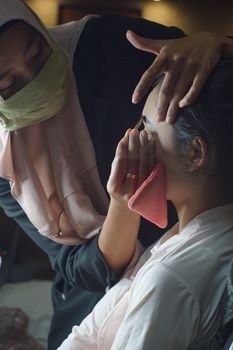 A makeup artist carefully applies cosmetics to a woman in an indoor setting, showcasing skillful artistry.