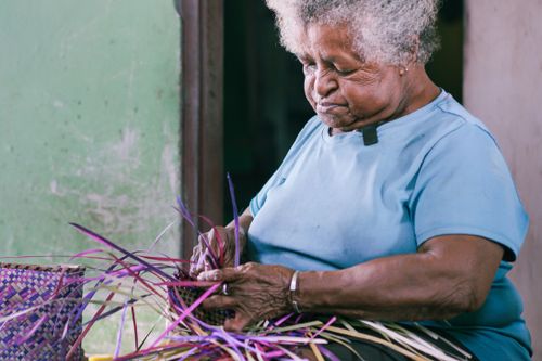 Free Senior woman skillfully weaving a basket using colorful threads, showcasing traditional craftsmanship. Stock Photo