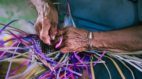 Close-up of senior hands skillfully weaving a colorful basket, highlighting traditional craftsmanship.