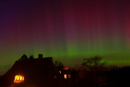 A stunning display of the aurora borealis casting colorful lights over a rural night landscape with lit cozy houses.