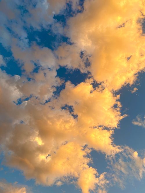 Free Dramatic golden clouds illuminated by sunset light against a blue sky, creating a serene atmosphere. Stock Photo