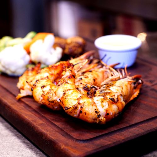 Free Delicious grilled shrimp served with vegetables and sauce on a wooden platter, perfect for seafood lovers. Stock Photo