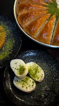 Close-up of Middle Eastern pastries and desserts topped with pistachios on a black plate.