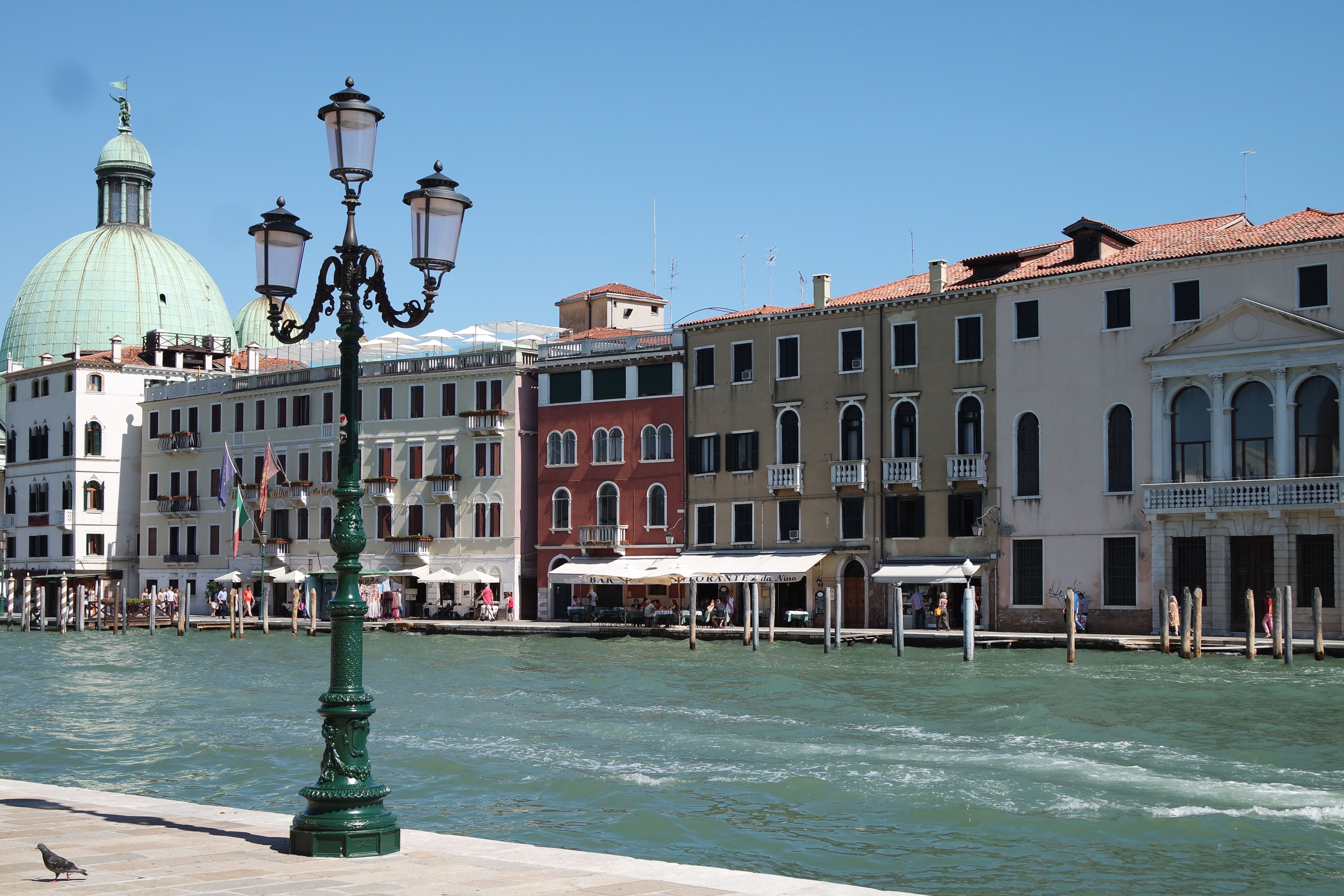 A picturesque view of Venice's canals with traditional buildings and a lamppost, under a clear blue sky.