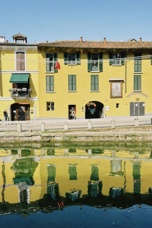 Free Yellow building with green windows reflects in a canal, creating a colorful scene on a sunny day. Stock Photo