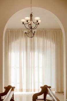 An elegant indoor archway with a chandelier and soft natural light filtering through sheer curtains.
