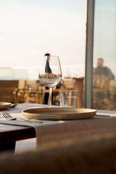 A stylish table setting with wine glass and plates at sunset, perfect for a fine dining experience.