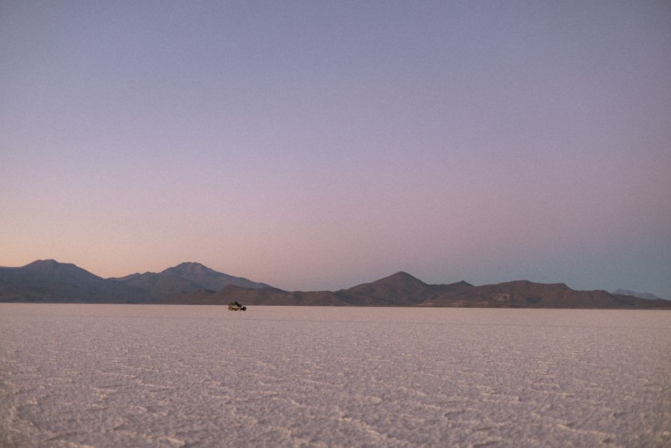 Breathtaking sunrise over Bolivia's Salar de Uyuni with a distant vehicle and mountain backdrop.