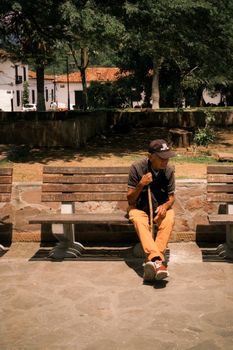 An elderly man with a cane sits on a bench under trees on a sunny day, exuding a peaceful, contemplative mood.