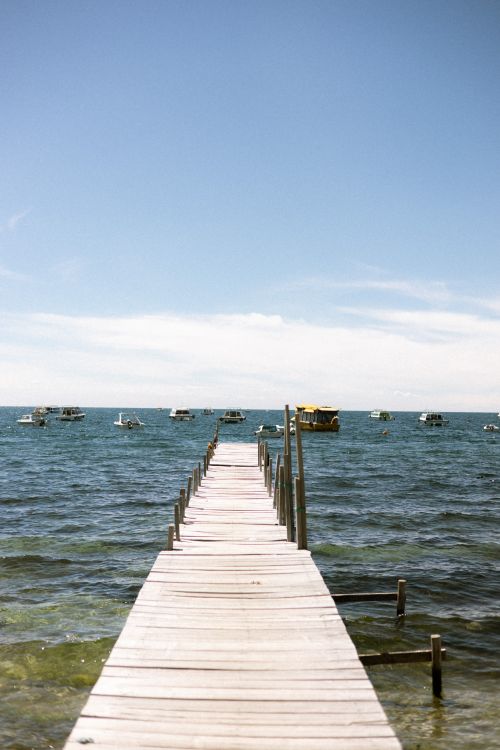 Free Wooden pier extending into Lake Titicaca with boats on the horizon under a clear blue sky in Copacabana, Bolivia. Stock Photo