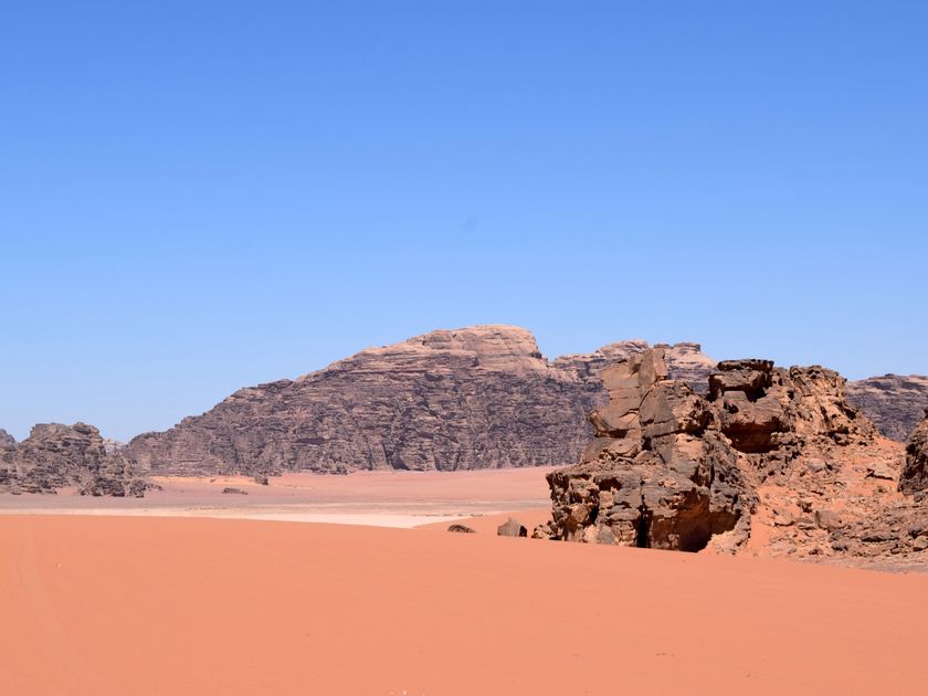 Vast dunes folding into sandstone formations under a clear sky