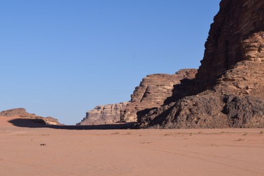 Expansive view of rocky desert terrain in Wadi Rum, showcasing towering cliffs under a clear blue sky.