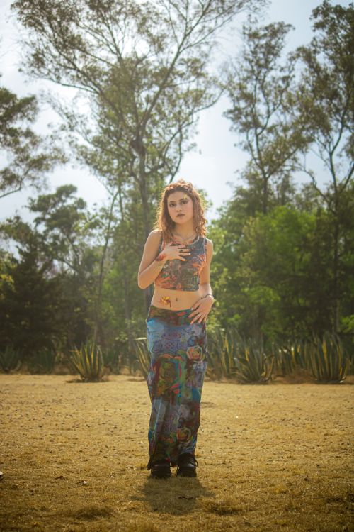 Free A woman in bohemian attire stands in a sunlit park, showcasing colorful fashion and floral accessories. Stock Photo