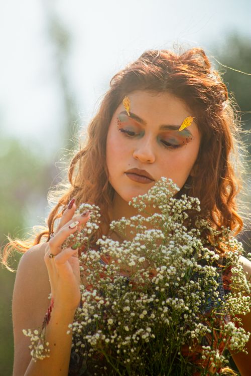 Free A young woman with artistic makeup admires flowers in a sunlit garden. Stock Photo
