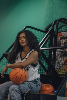 Young woman with curly hair holding a basketball indoors, showcasing confidence.