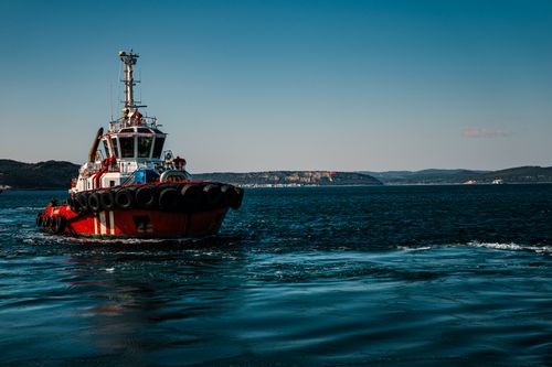 Free A vibrant red tugboat navigates the blue waters of Çanakkale, Türkiye, under a clear sky. Stock Photo