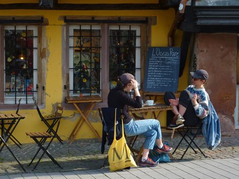 Two people relaxing at an outdoor cafe table in a European town, enjoying conversation and coffee.