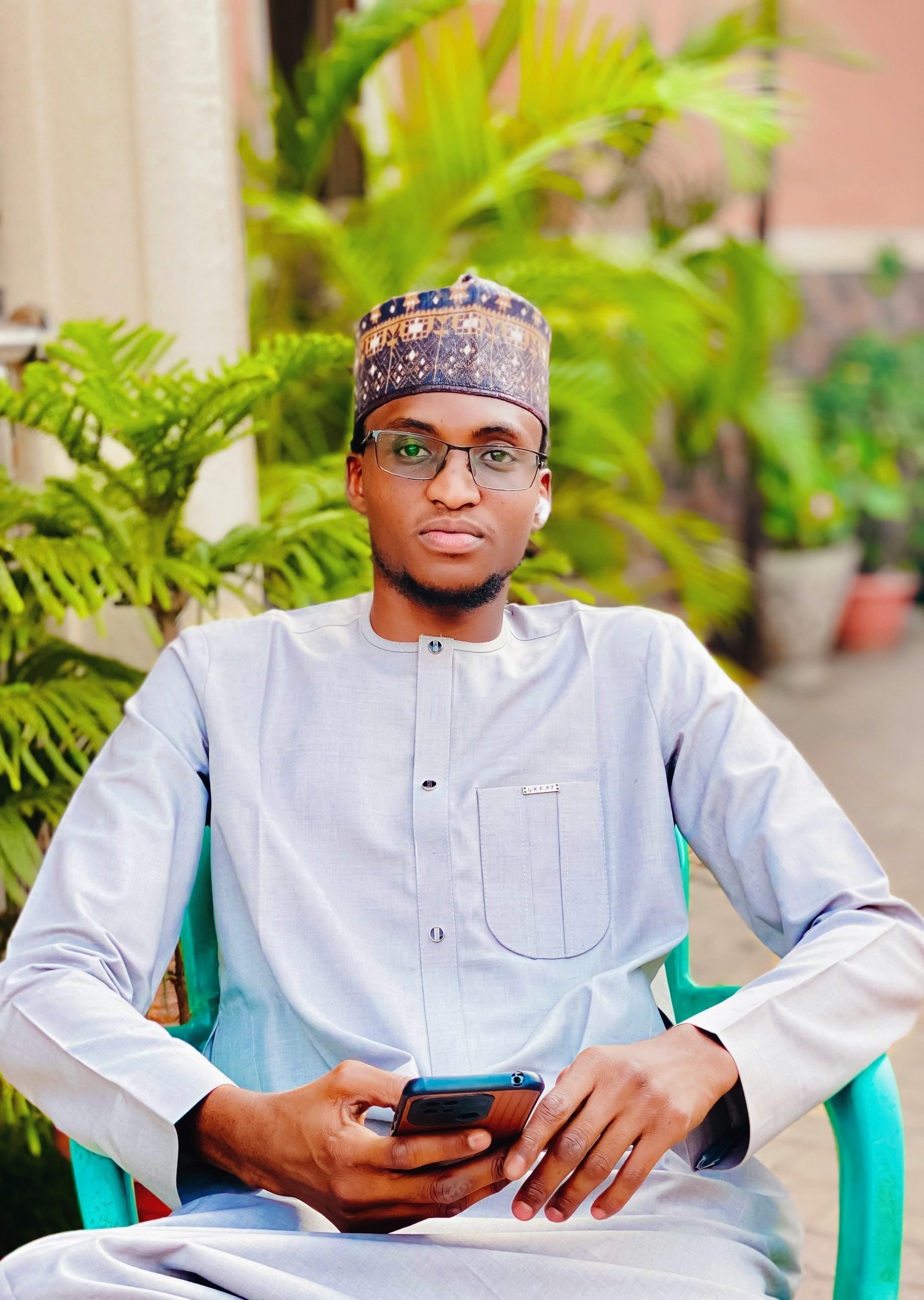 Young man in stylish attire sitting outdoors holding a smartphone.