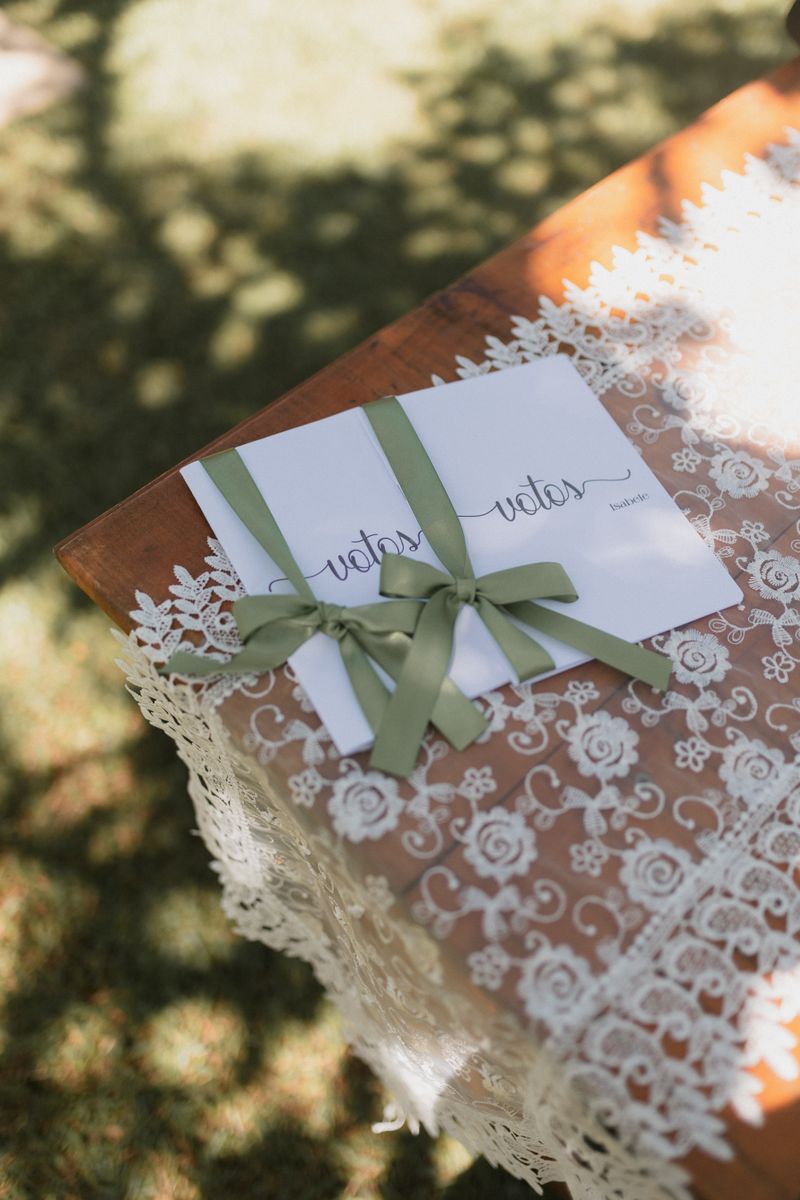 Wedding vow booklets tied with a green ribbon resting on a lace-covered table outdoors, embodying elegance.