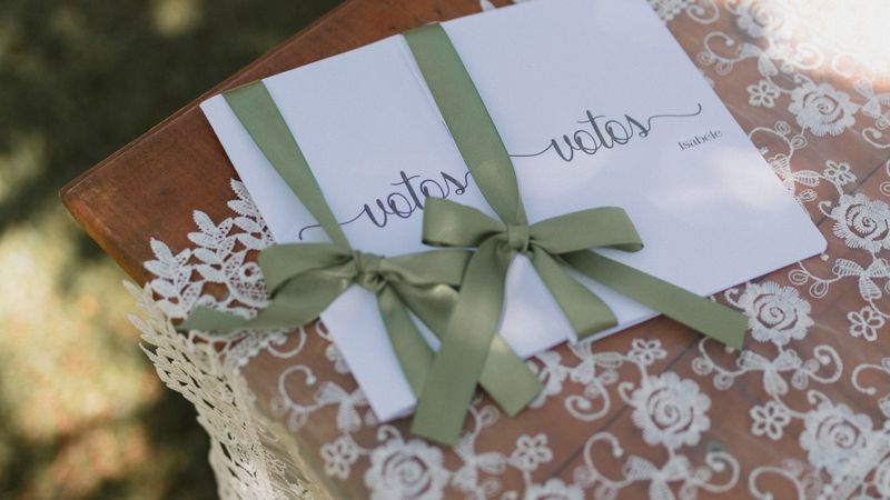 Wedding vow booklets tied with a green ribbon resting on a lace-covered table outdoors, embodying elegance.