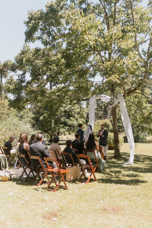 Free A serene outdoor wedding ceremony set in a lush garden under a tree with guests seated. Stock Photo