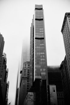 Black and white photo of a modern skyscraper in a city skyline on a foggy day.