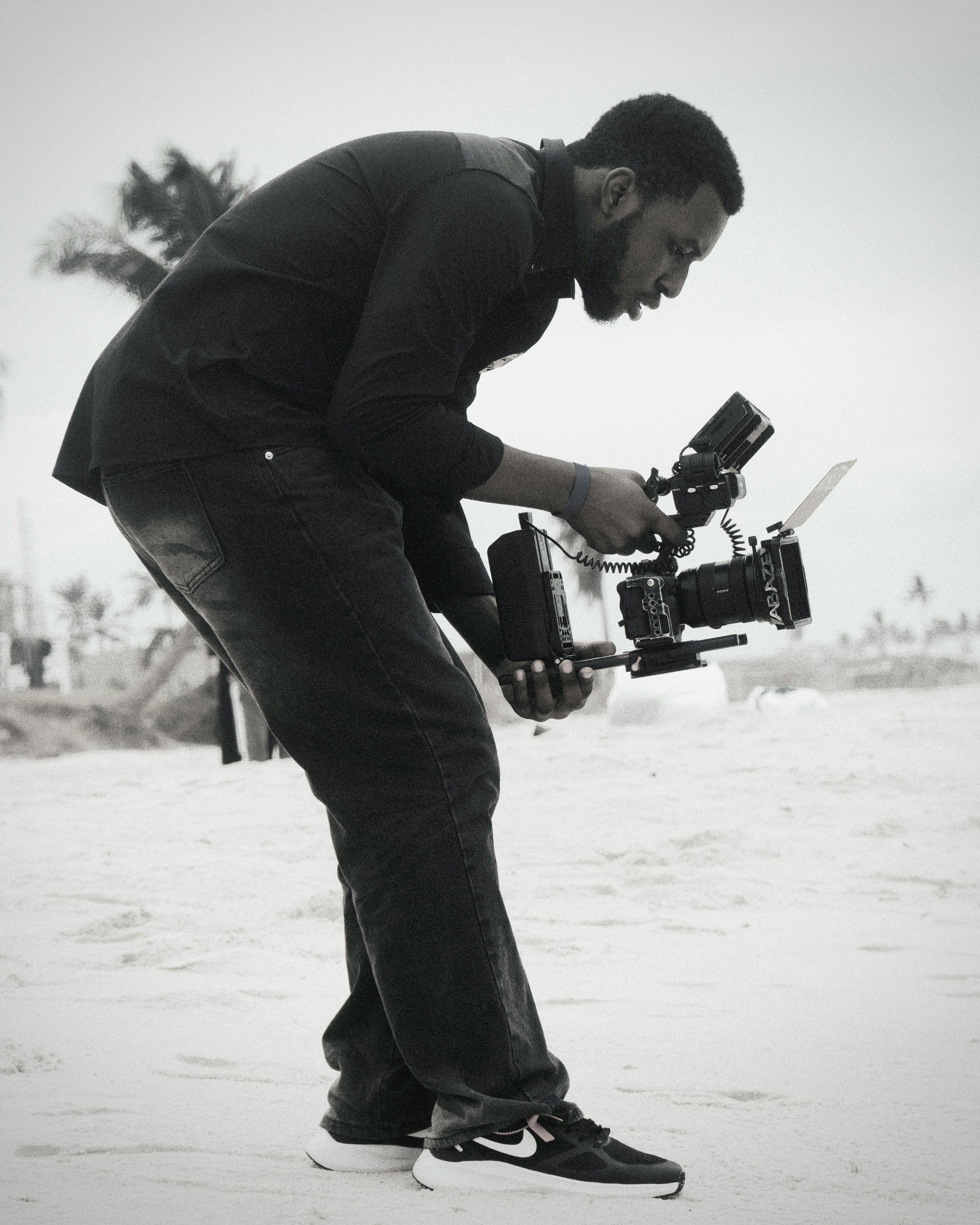 A videographer with camera equipment capturing footage on a sandy beach.